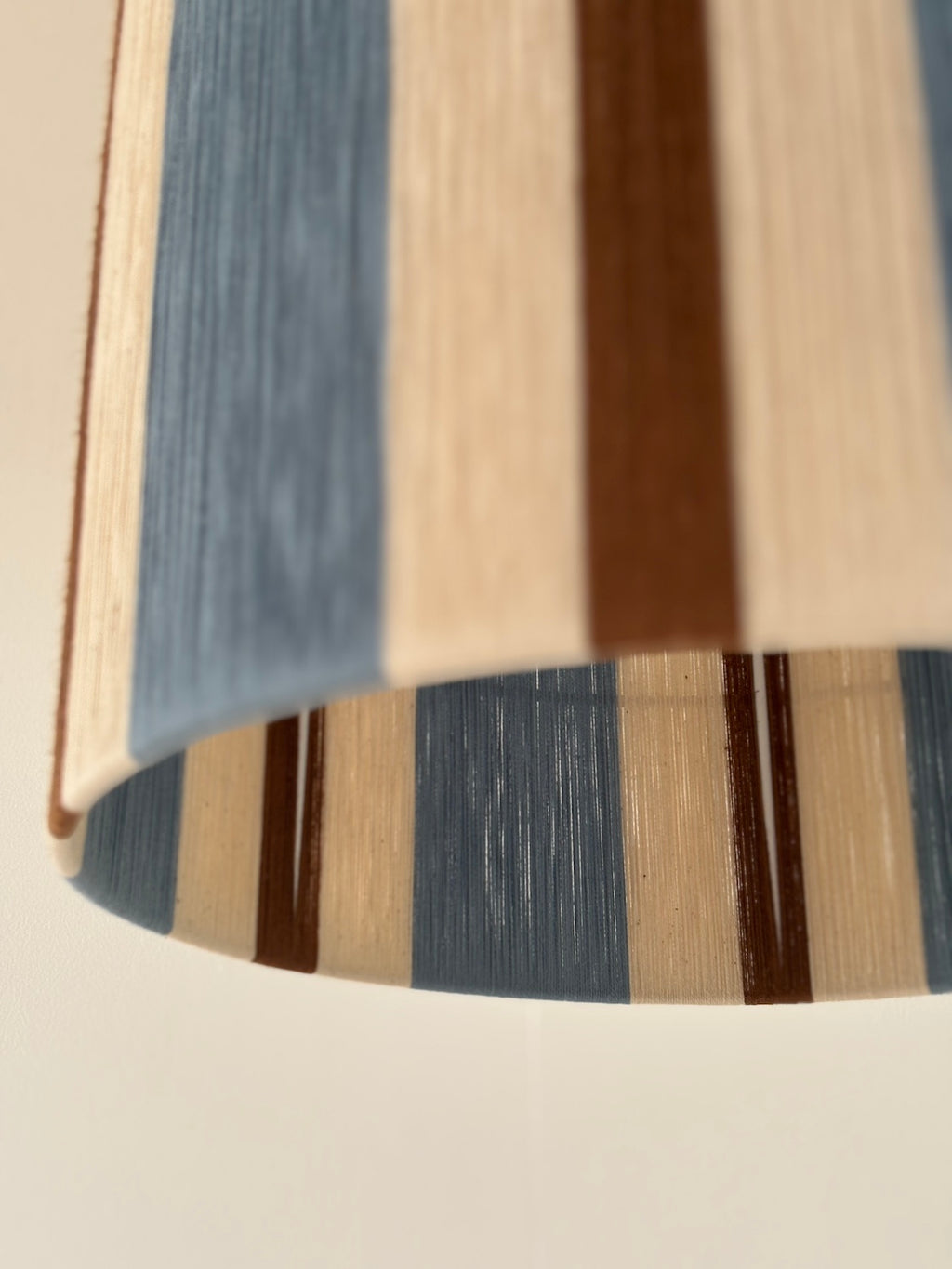 Close-up view of the Cléo Drum pendant light, showing handwoven vertical stripes in cloud blue, natural and fawn yarn