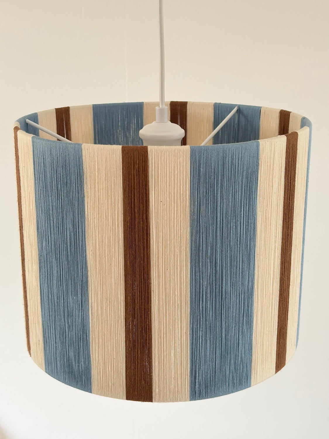 Top view of the Cléo Drum Small pendant light, showing handwoven vertical stripes in cloud blue, natural and fawn yarn