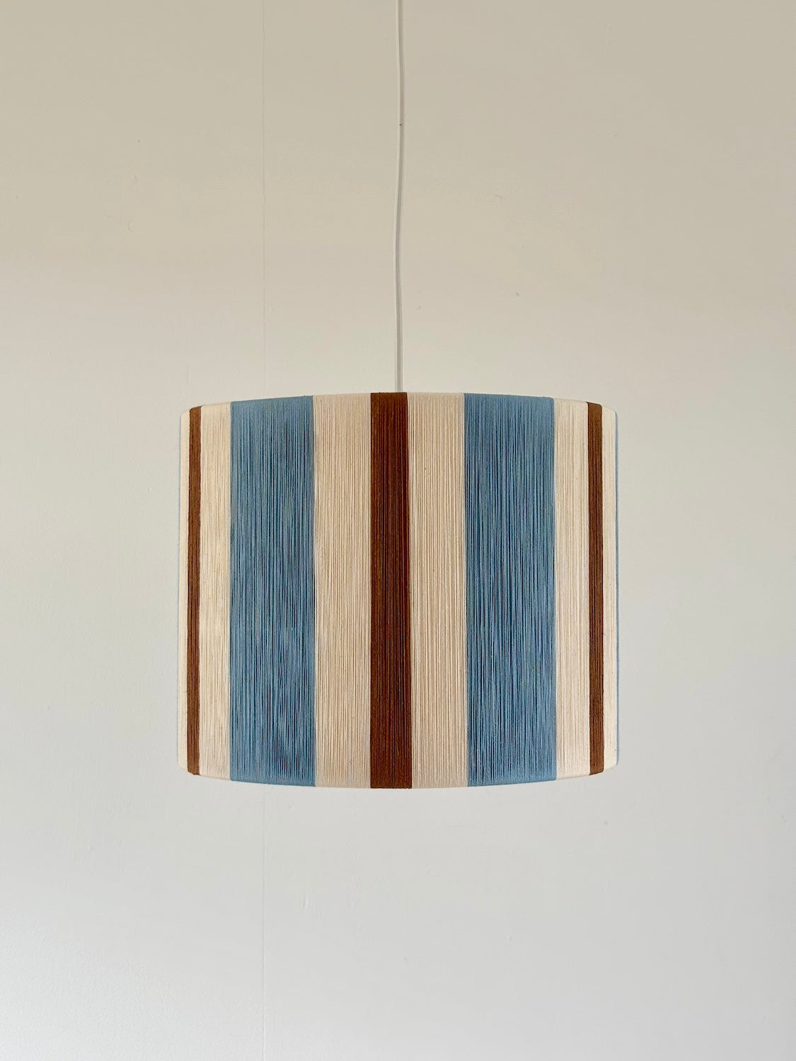 Cléo Drum pendant light with handwoven vertical stripes in cloud blue, natural and fawn yarn.
