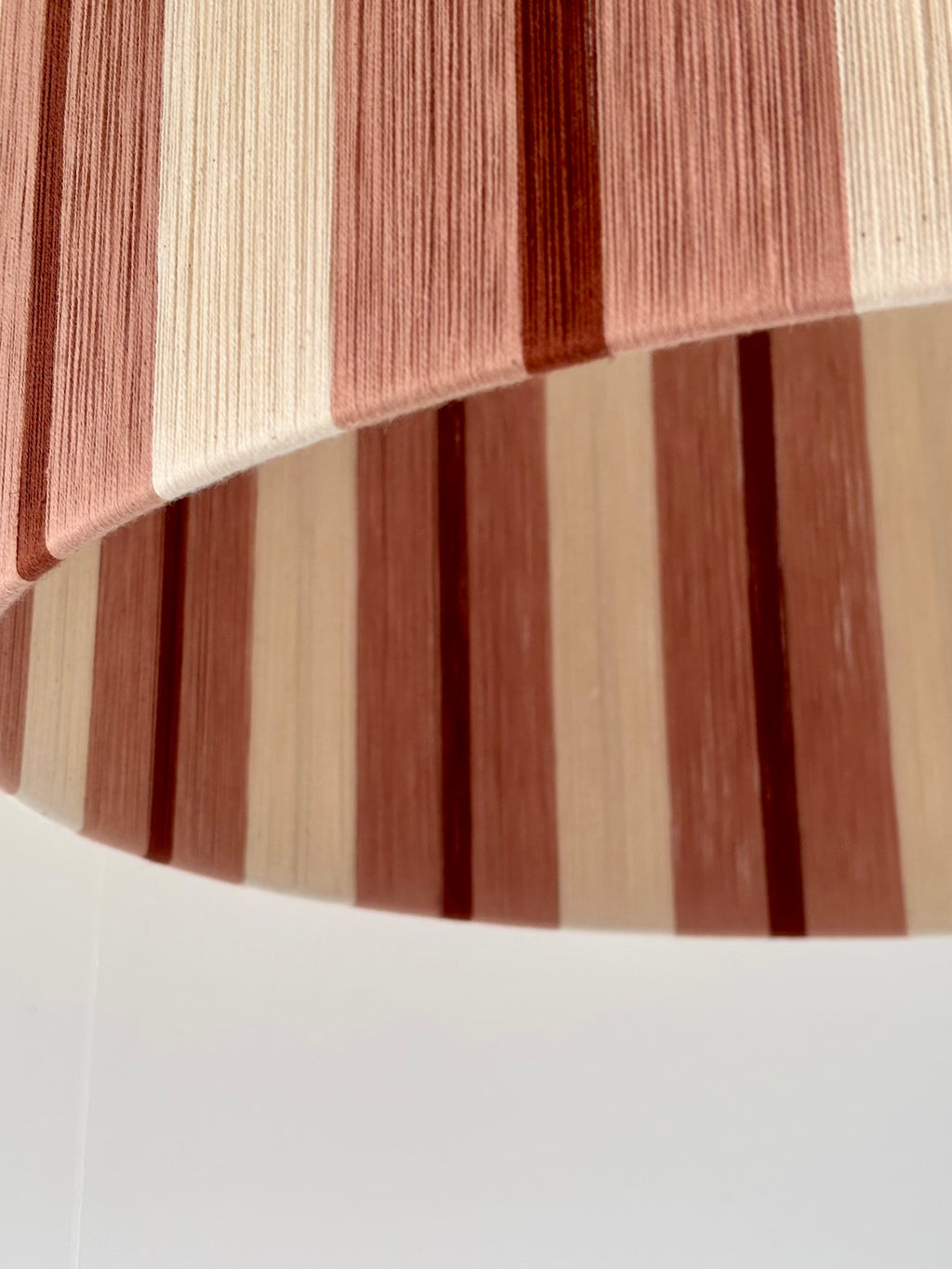 Lower edge of the Marnie Drum Large pendant, showing handwoven cinnamon and natural vertical yarn stripes