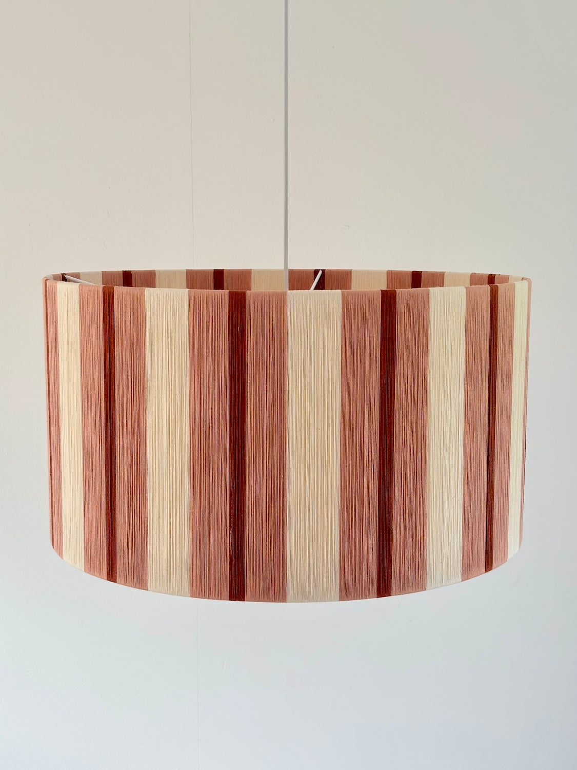 Front view of the Marnie Drum Large handwoven pendant light in cinnamon, light brick red and natural stripes