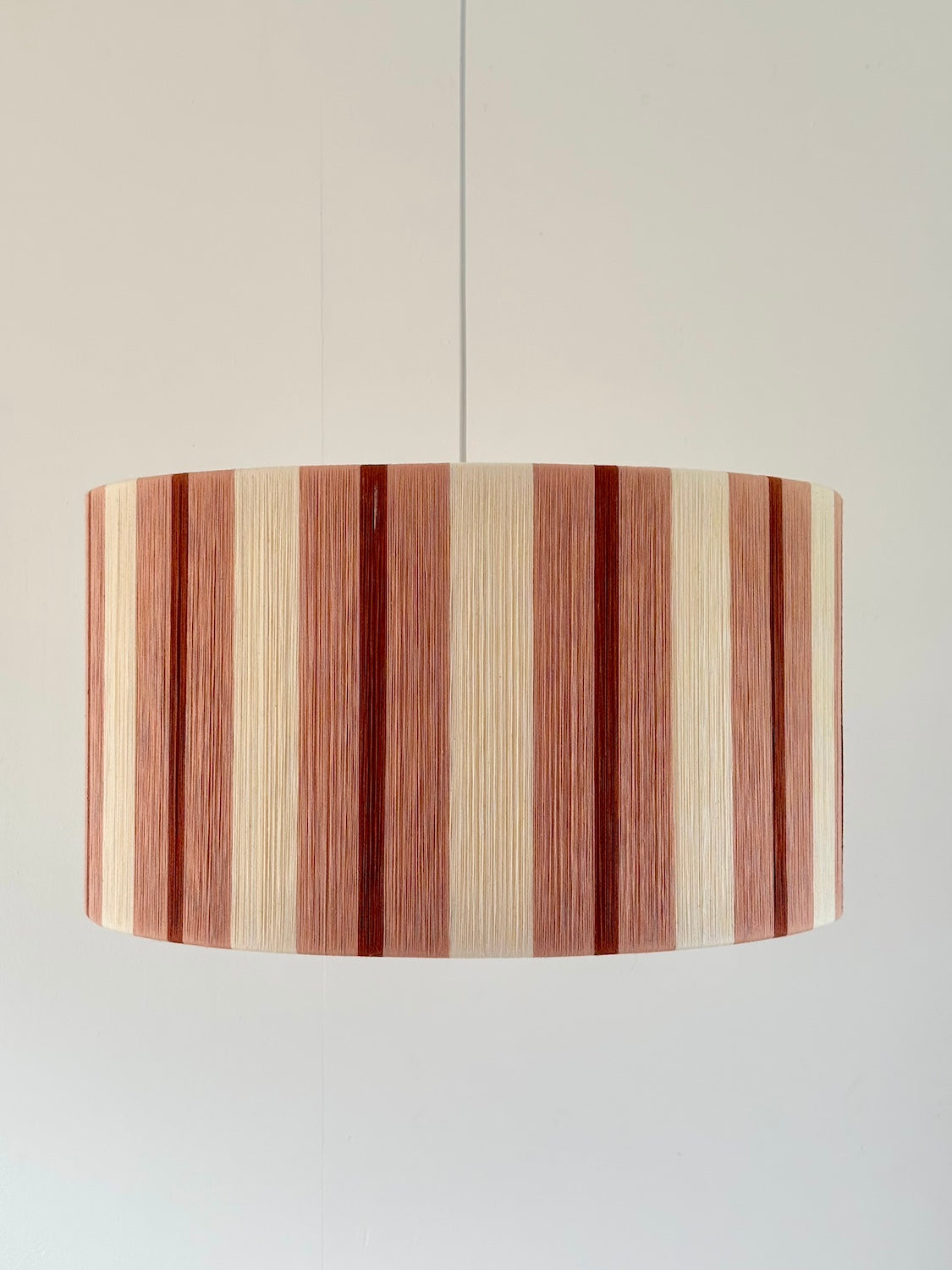 Front view of the Marnie Drum Large handwoven pendant light in cinnamon, light brick red and natural stripes