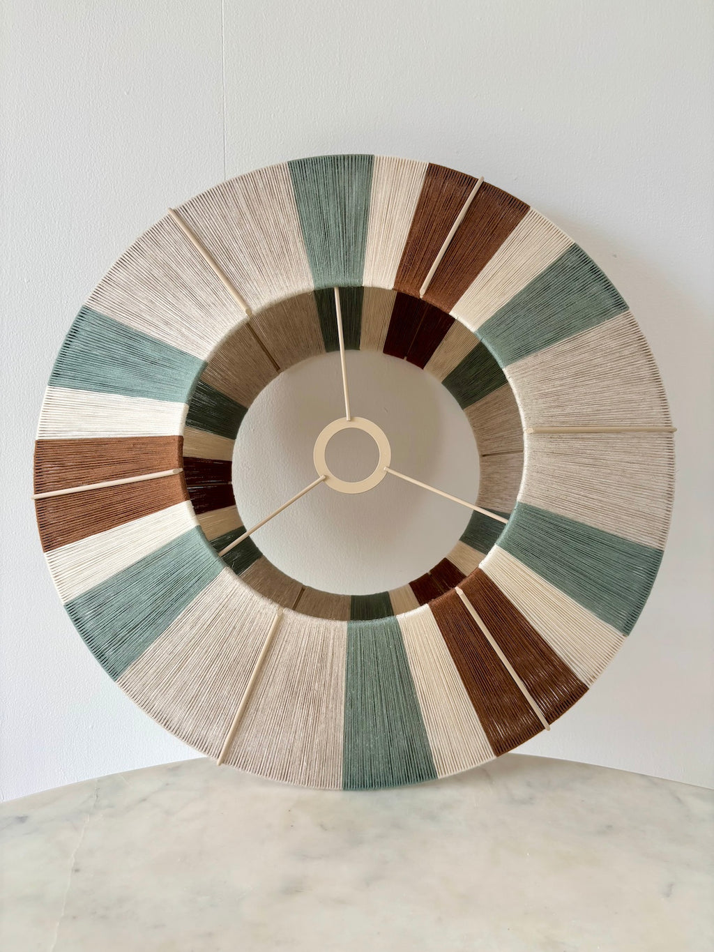 View of the Sarto Orb leaning against a wall, revealing its geometric form and sage, natural and fawn woven stripes.