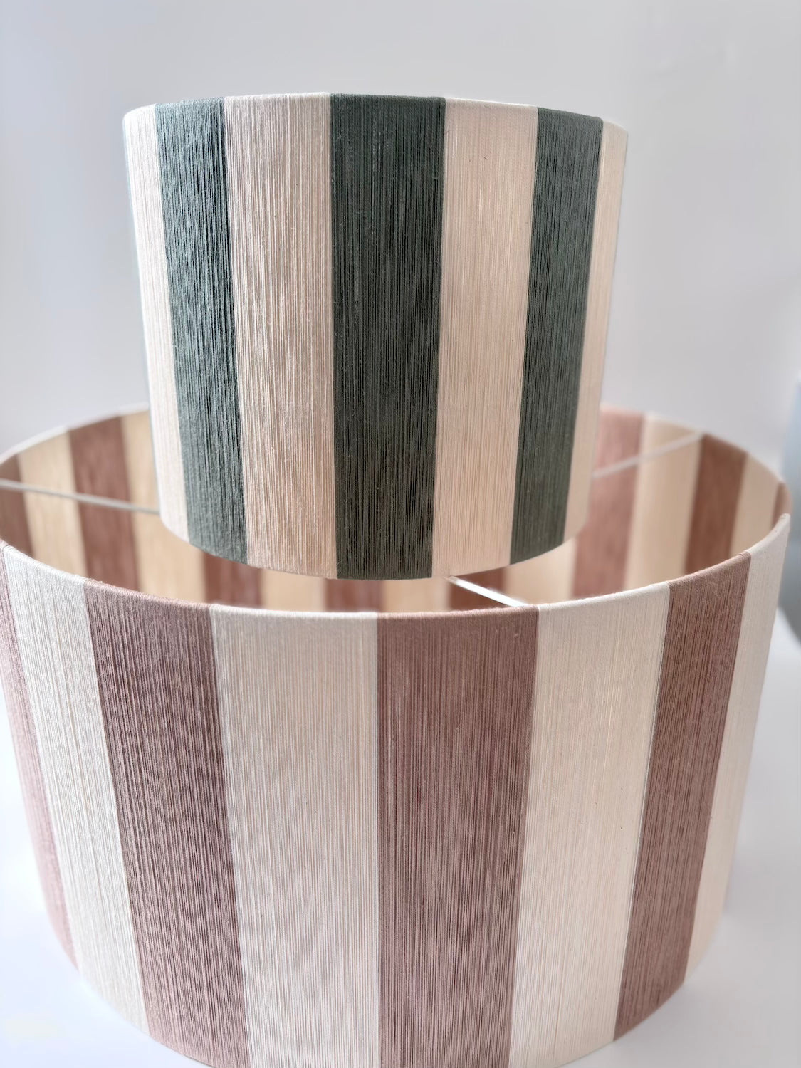 Handwoven small and large drum pendant light with beige and sage horizontal stripes, designed by Skye Lightly.