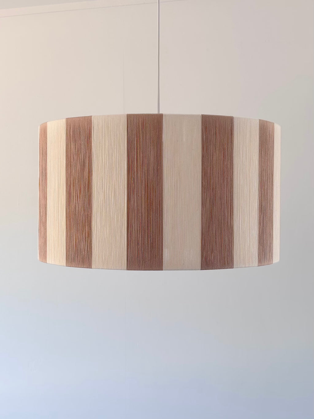 front view of handwoven drum pendant light with beige and natural stripes by Skye Lightly.
