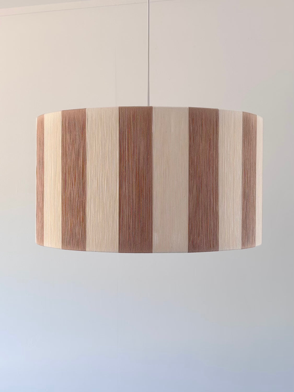 front view of handwoven drum pendant light with beige and natural stripes by Skye Lightly.