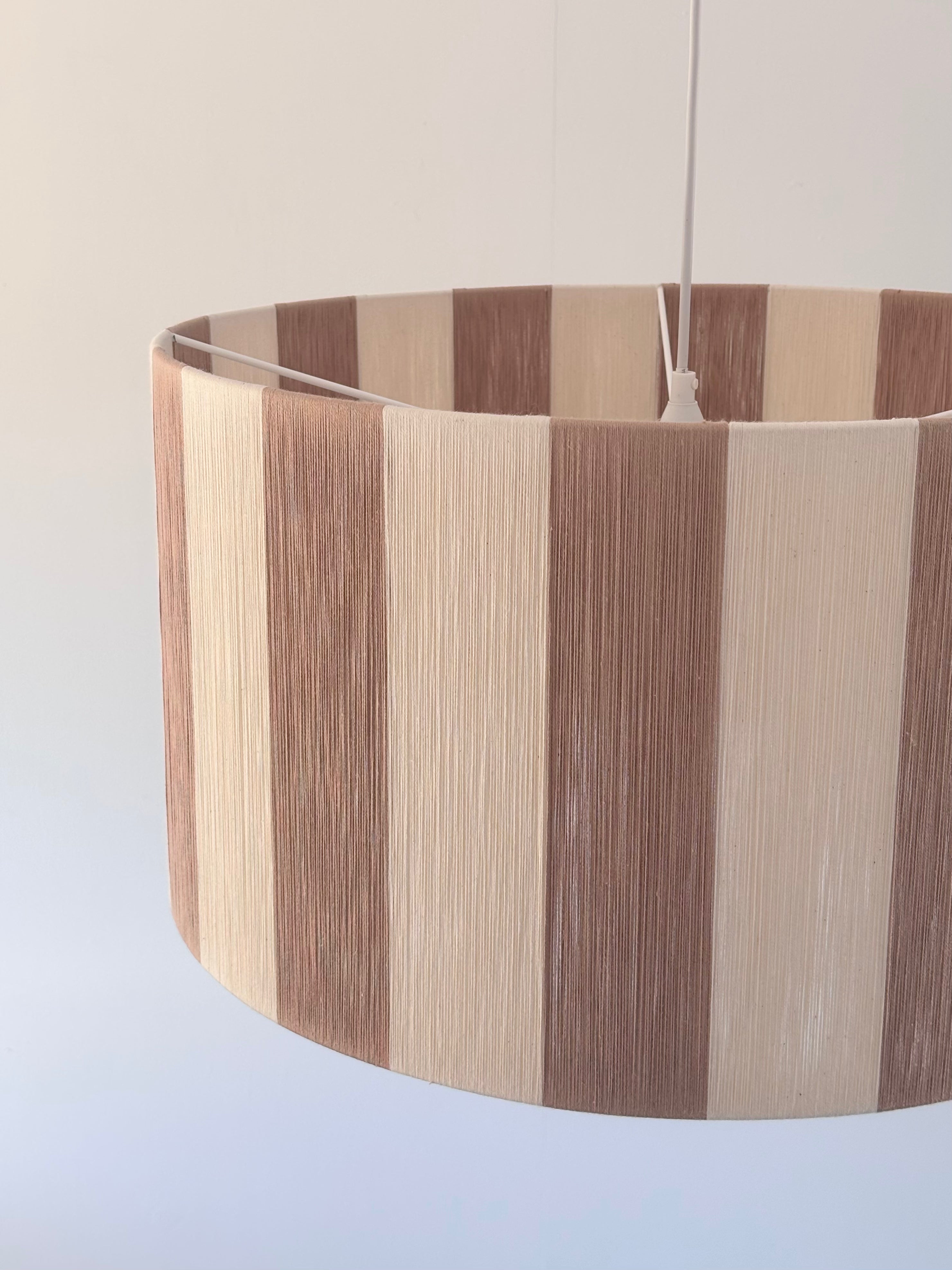Side view of handwoven drum pendant light with beige and natural stripes by Skye Lightly.