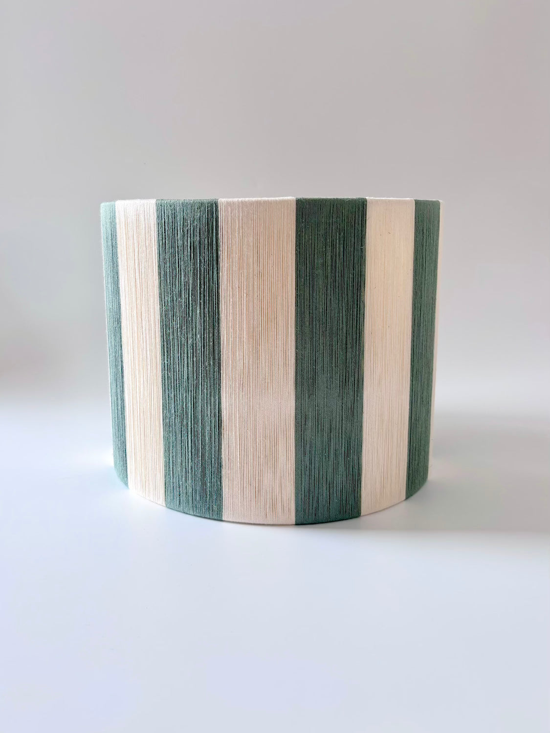Front view of handwoven drum pendant light with sage and natural stripes by Skye Lightly.