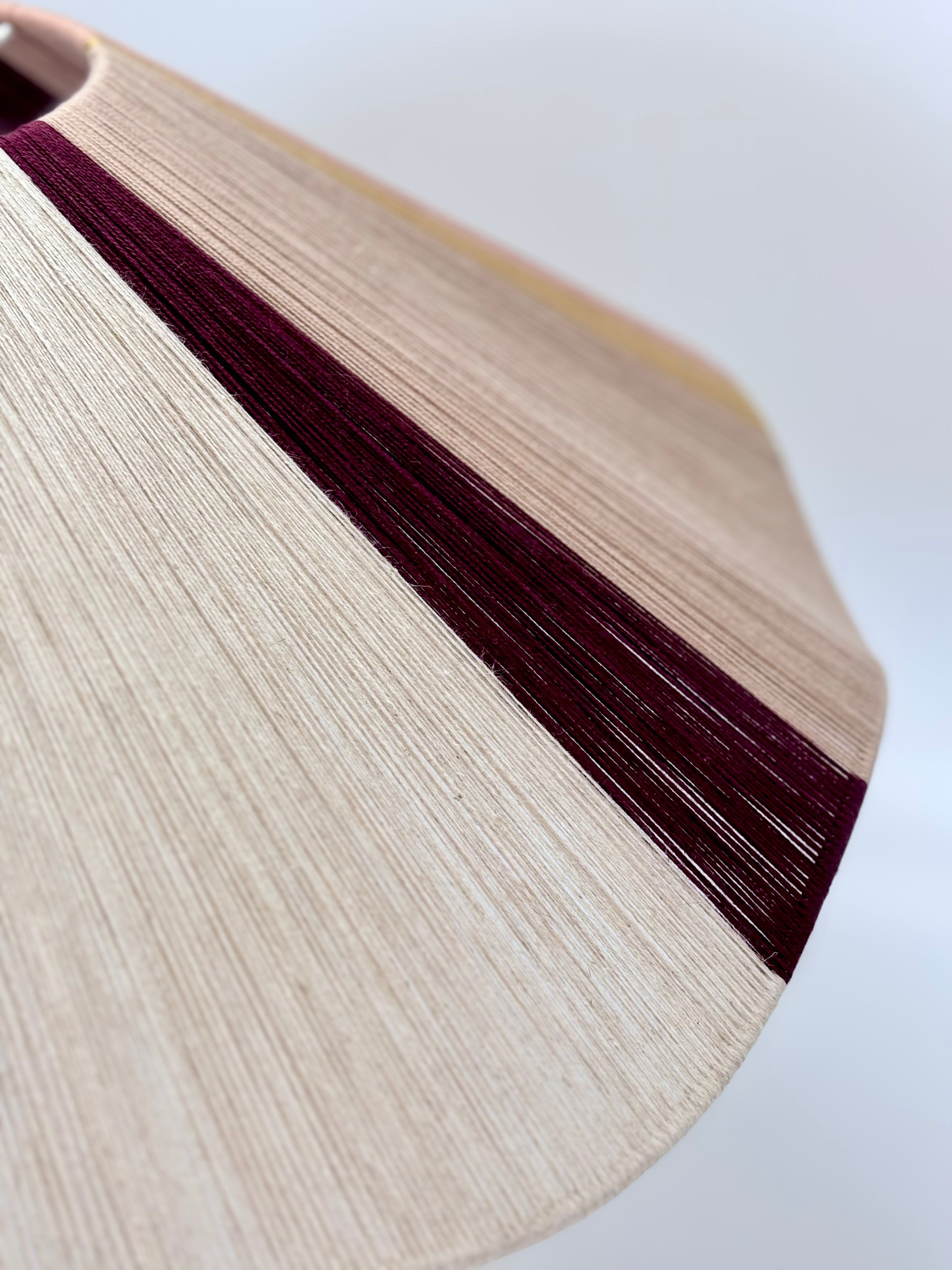 closeup of handwoven cottesloe Wave pendant light in burgundy, blush, gold and natural yarns by Skye Lightly.