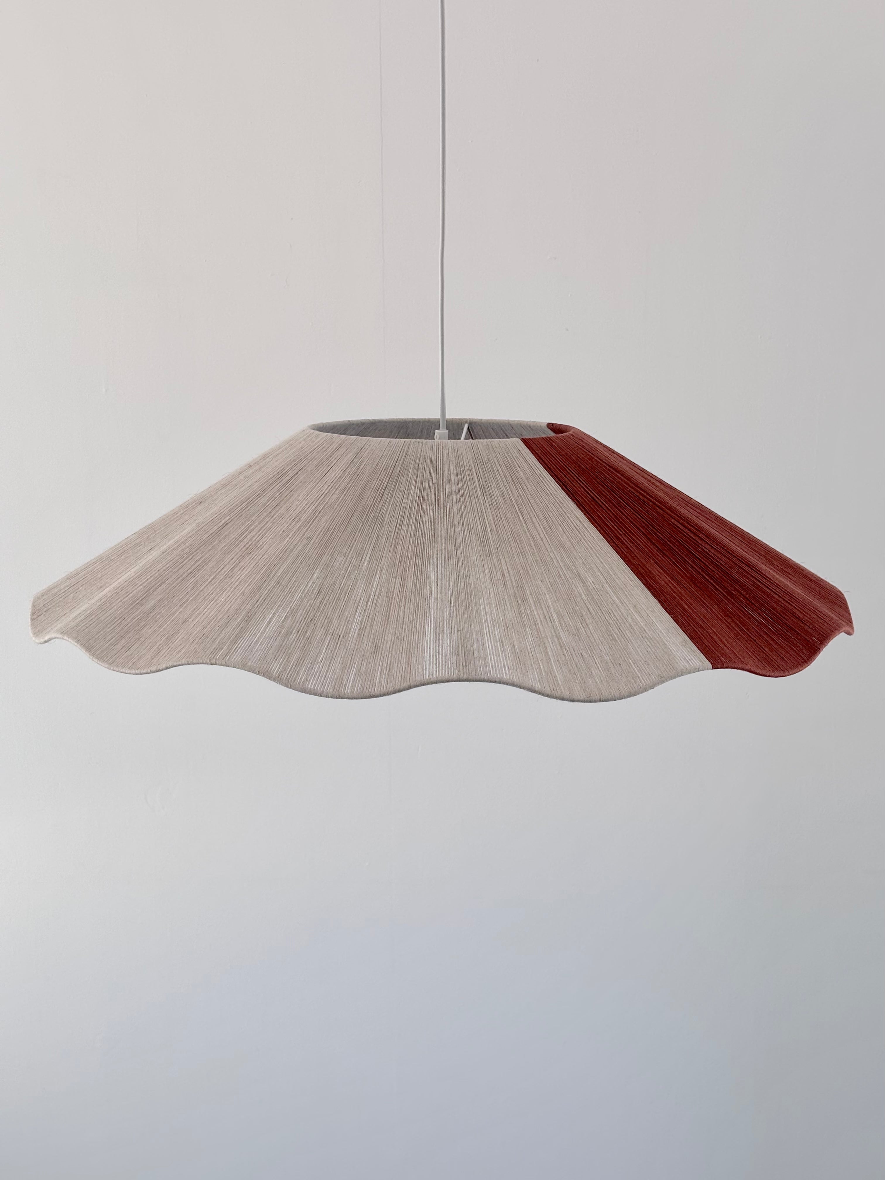 A pendant lamp with a natural linen and red color block yarn design, hanging against a white background.