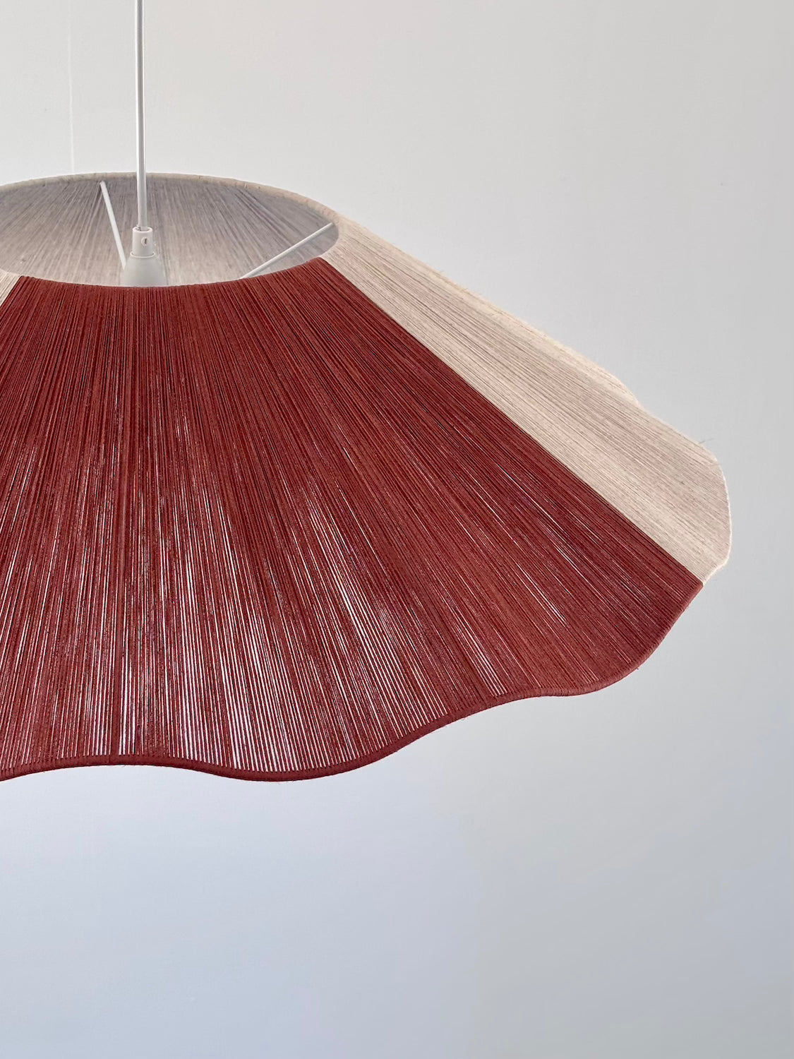 side closeup view of a pendant lamp with a natural linen and red color block yarn design, hanging against a white background.