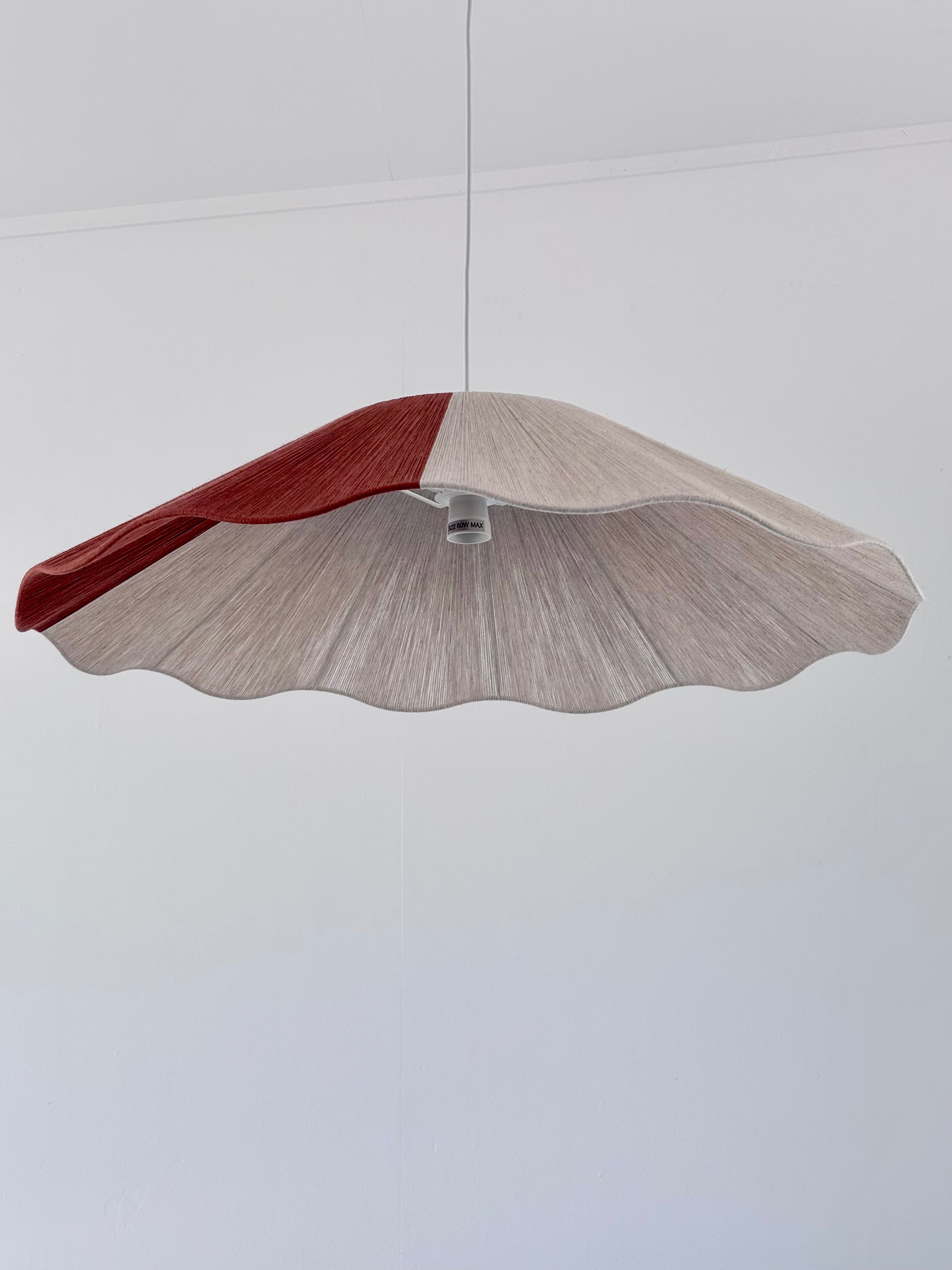 A pendant lamp with a natural linen and red color block yarn design, hanging against a white background.