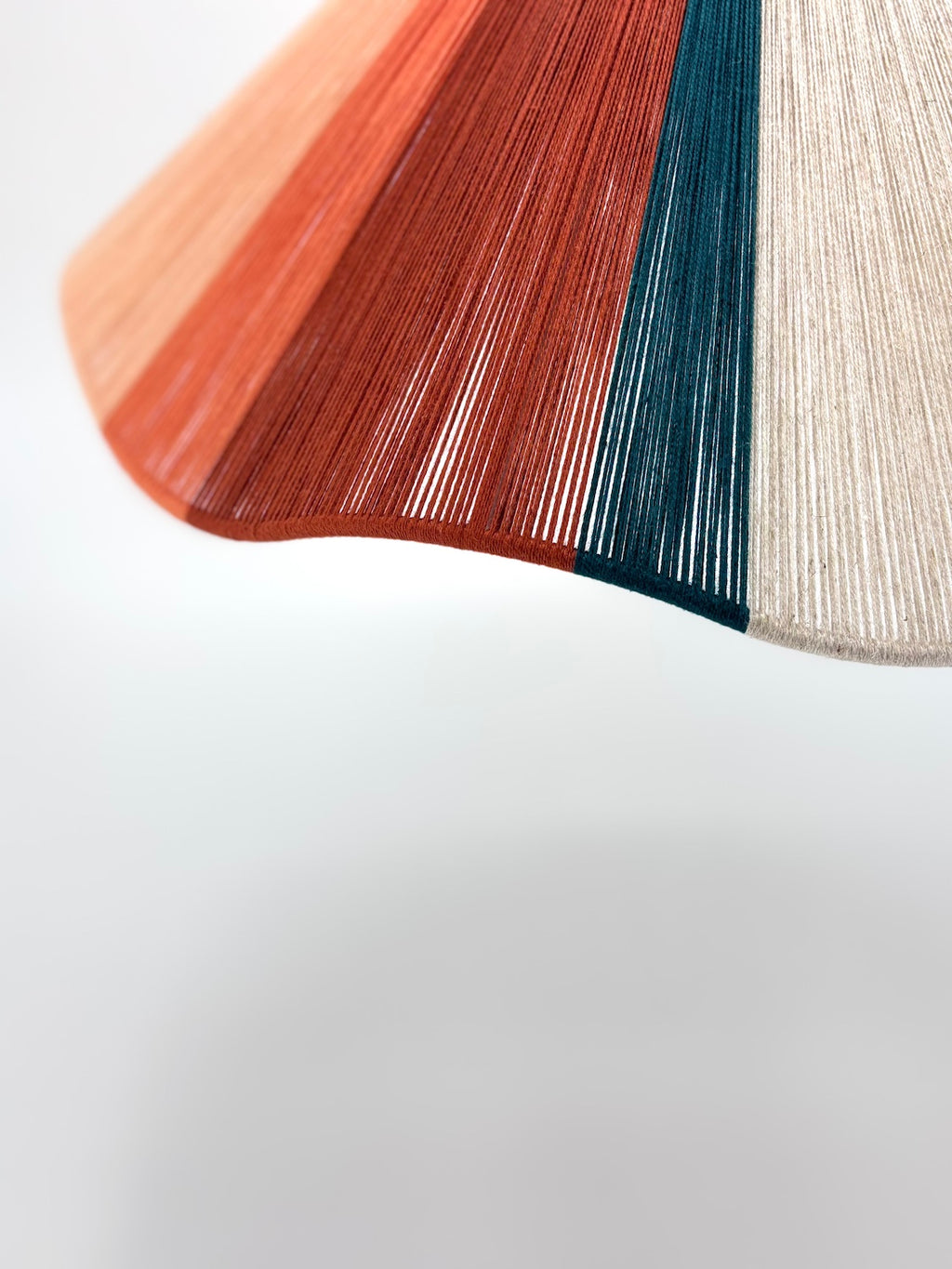 closeup of venice Wave pendant light handwoven in peach, teal, burgundy and natural yarns by Skye Lightly.