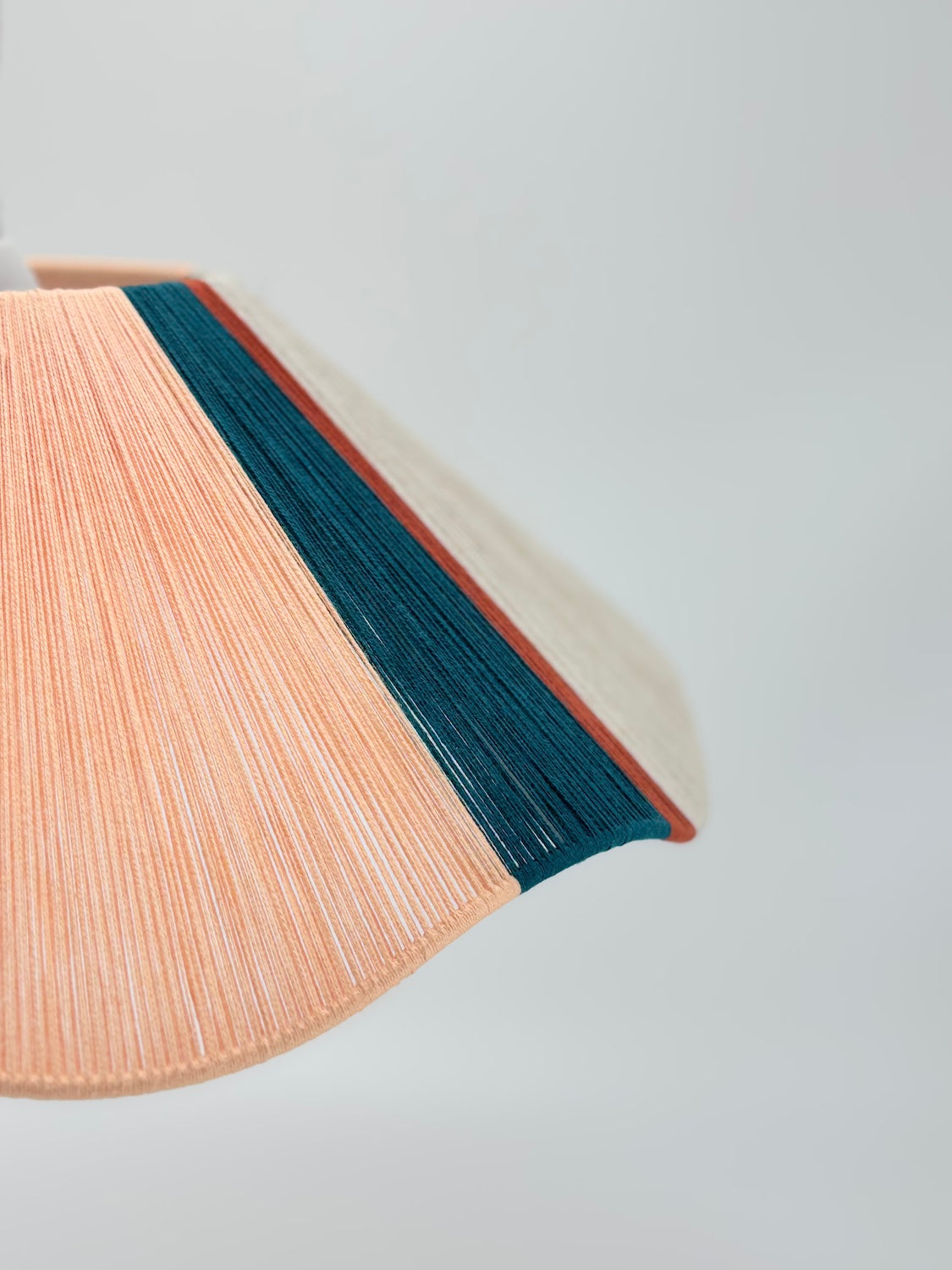 side view of venice Wave pendant light handwoven in peach, teal, burgundy and natural yarns by Skye Lightly.